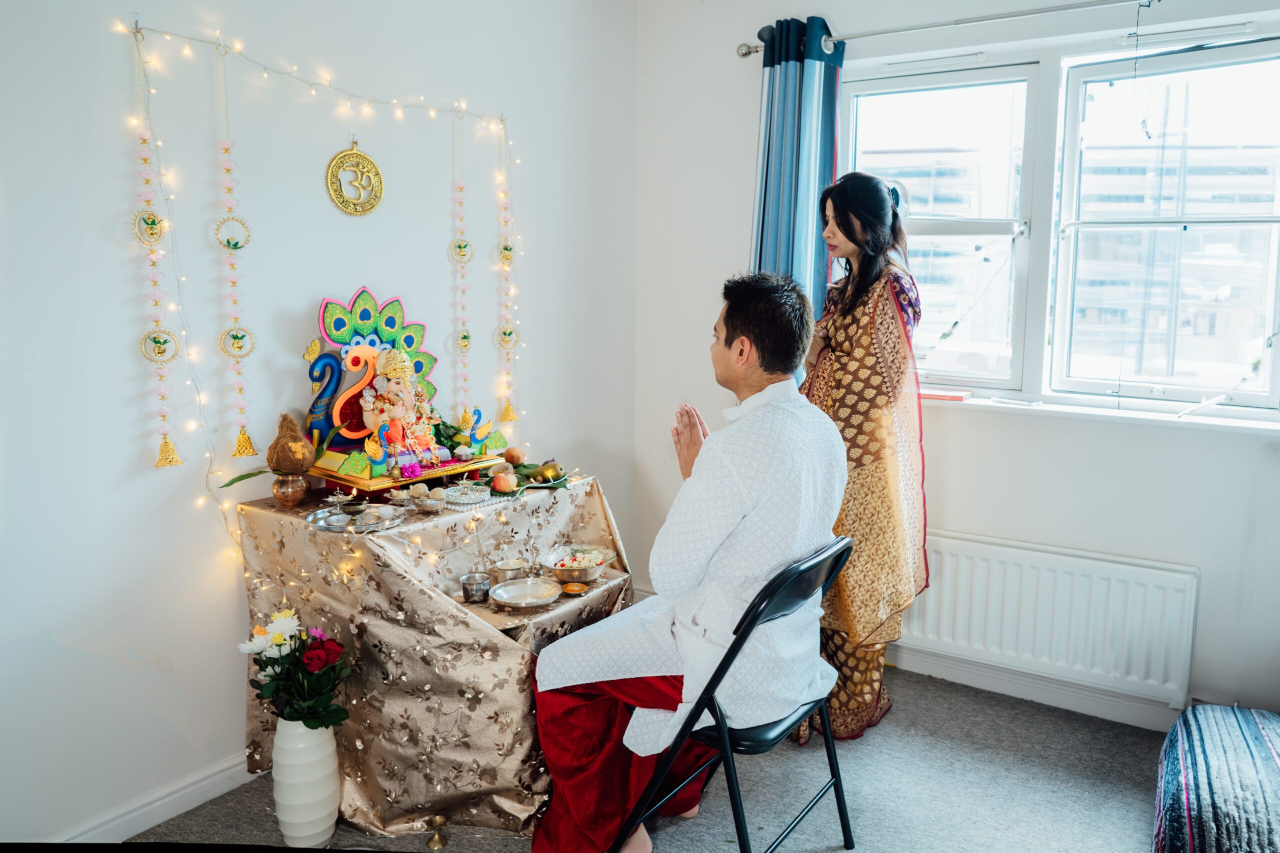 Indian couple dressed in traditional wear engages in worship at home altar, adorned with decors and offerings for god Ganesh during festive celebration. Indian culture, hindu ritual and customs. Indian couple dressed in traditional wear engages in worship at home altar, adorned with decors and offerings for god Ganesh during festive celebration. Indian culture, hindu ritual and customs