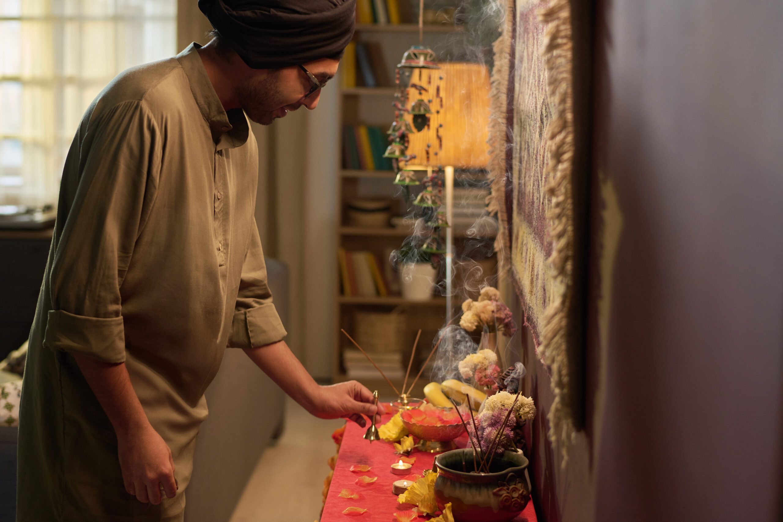 Man Preparing Religious Altar in Cozy Indoor Setting Man preparing religious altar with yellow candles and flowers in cozy indoor space. Focused and reverent setting displaying rituals and cultural practices